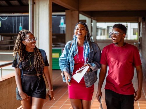 A group of black students in their 20's walking through a corridor on campus talking to each other and laughing.