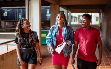 A group of black students in their 20's walking through a corridor on campus talking to each other and laughing.